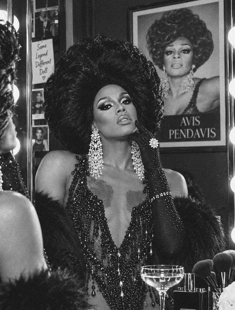 Dee Jiles at a vanity beside a framed portrait of Avis Pendavis